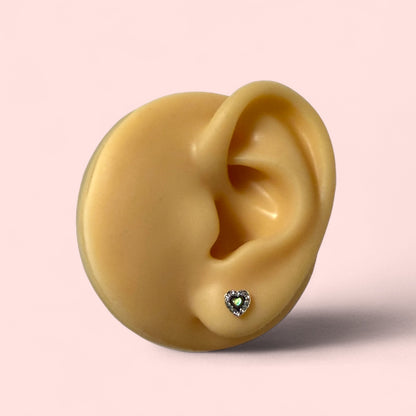 Gold heart-shaped earring on a detailed model of an ear with a pink background