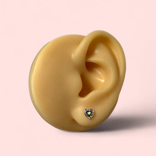 Gold heart-shaped earring on a detailed model of an ear with a pink background
