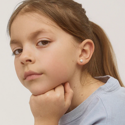 Young girl with a ponytail wearing a pearl earring against a plain background
