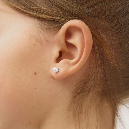 Close-up of an ear wearing a pearl stud earring with hair partially covering the frame.
