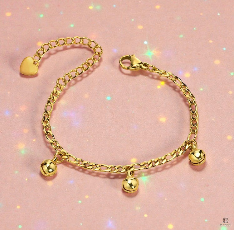 Children's anklets made of gold ion plated 316L surgical steel with musical bell charms on a pink background.