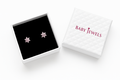 High-resolution product shot of a white quilted jewellery box and its matching lid on a white background; the open box reveals a black velvet interior holding a pair of rose-gold star-shaped earrings set with pink cubic zirconia, while the quilted lid beside it is embossed with the ‘BABY JEWELS’ logo in burgundy.