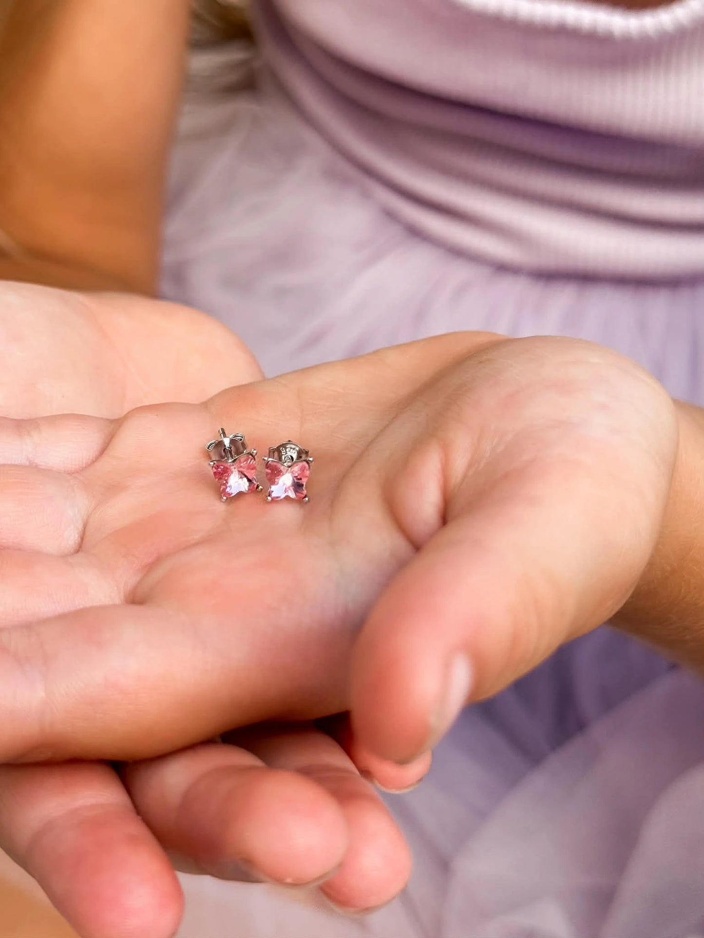 Children's earrings featuring 925 sterling silver pink Austrian crystal butterfly studs in a child's hand.
