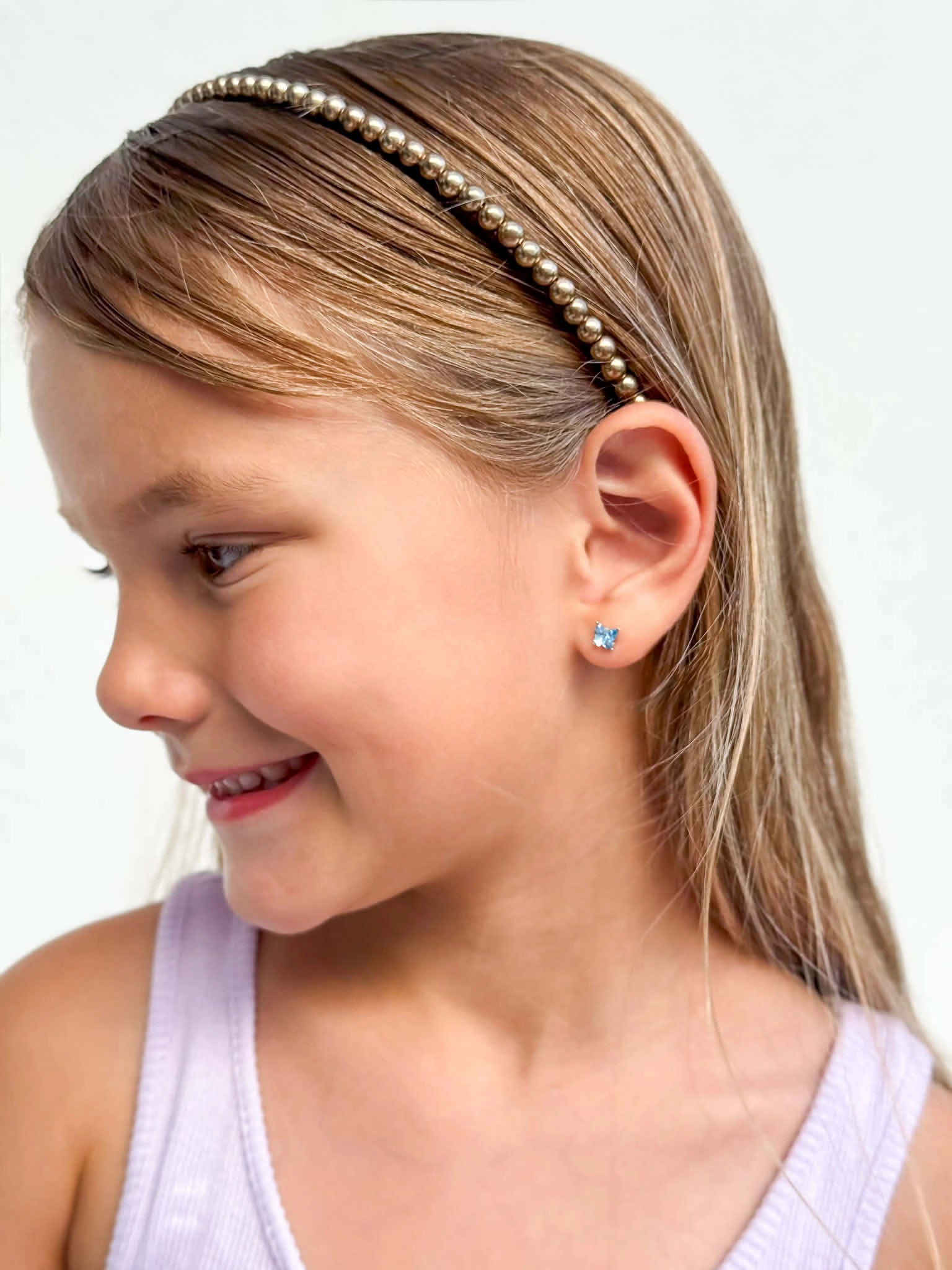 Smiling girl wearing 925 sterling silver children's earrings with blue Austrian crystal butterfly studs and a pearl headband.