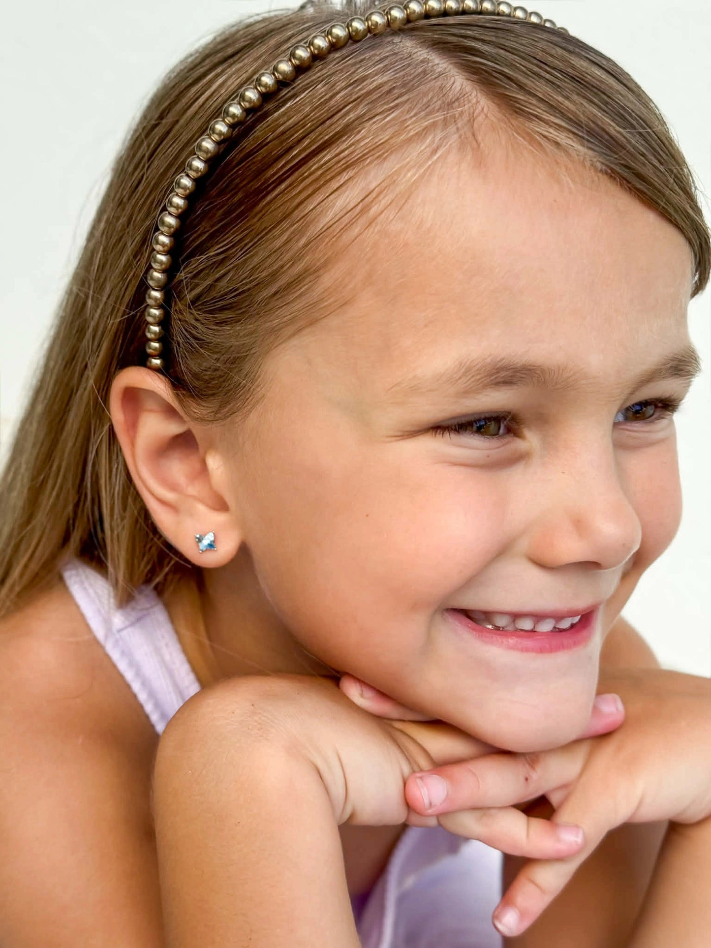 Child wearing children's earrings with blue Austrian crystal butterfly studs, smiling with a headband.