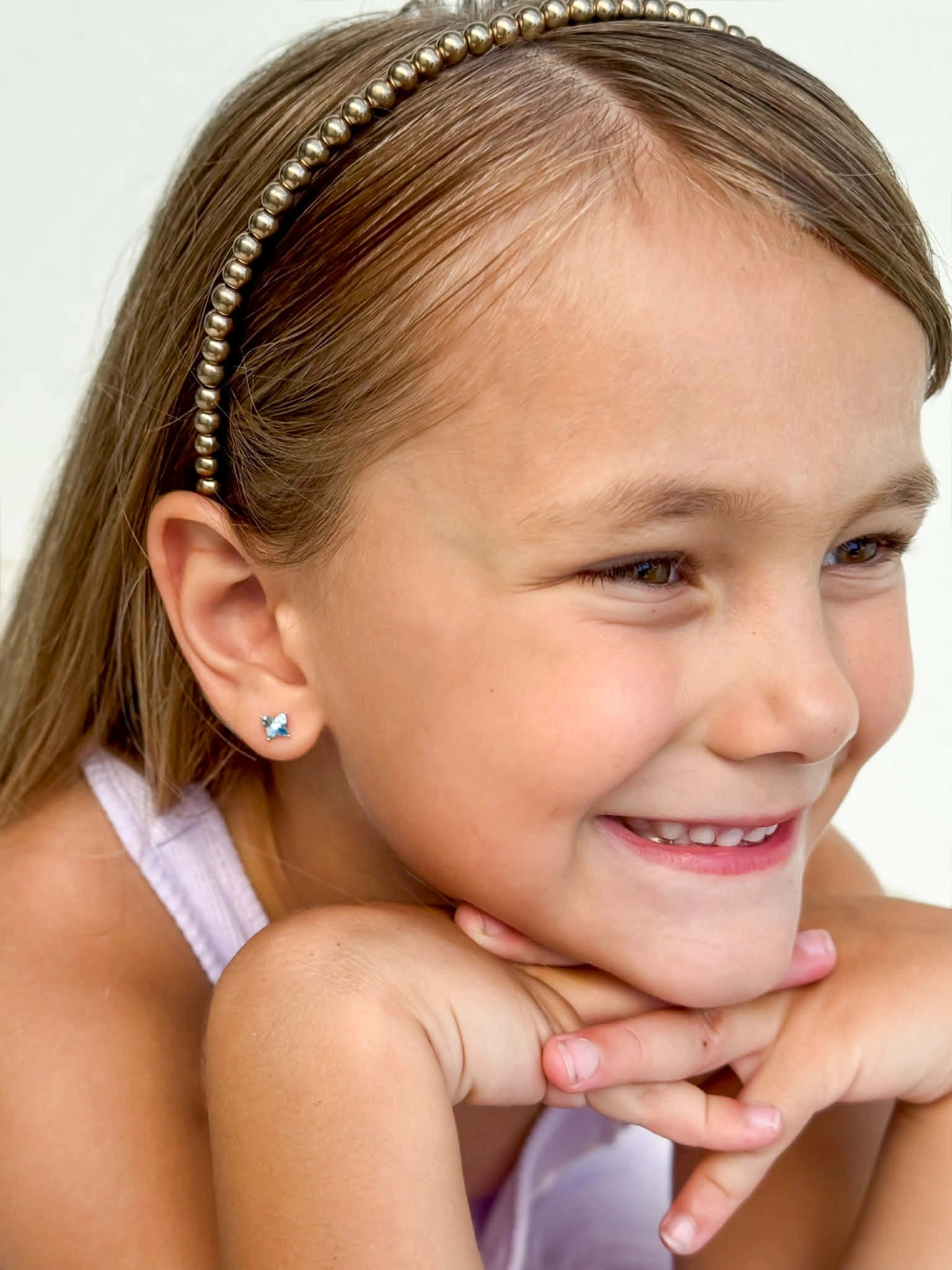 Child wearing children's earrings with blue Austrian crystal butterfly studs, smiling with a headband.