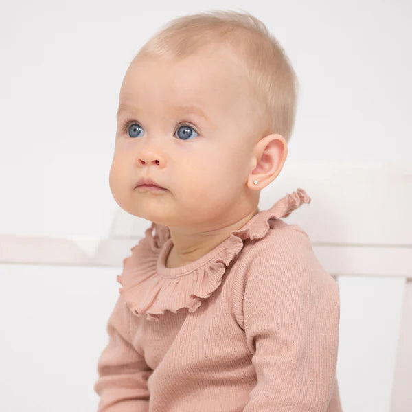 Adorable baby wearing a pink sweater with ruffles, showcasing cute earrings.