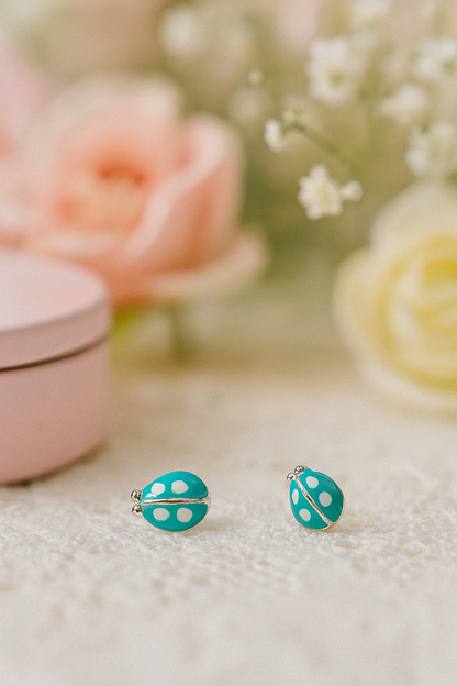 Turquoise polka dot earrings on a textured surface with blurred flowers and pink box in the background