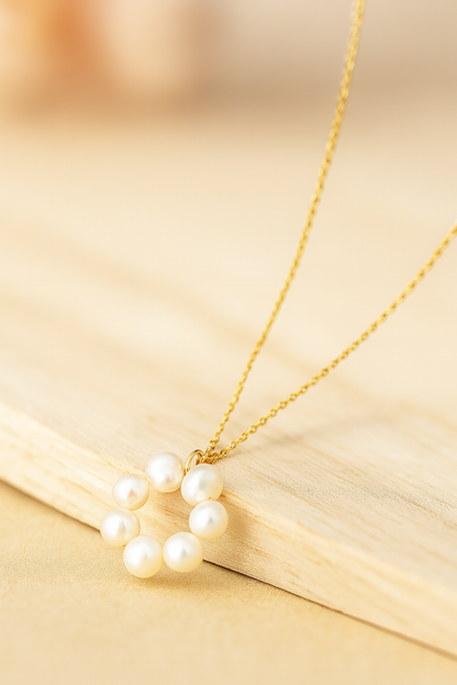 Gold necklace with a circular pendant made of white pearls, shown on a warm, neutral lifestyle background.