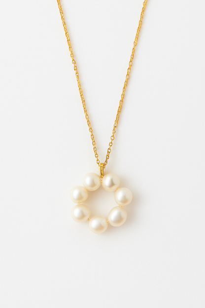Gold necklace with a circular pendant made of white pearls, laid flat on a plain white background.