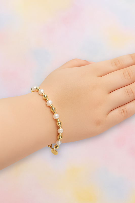 A child's hand wearing a pearl and gold bead bracelet, resting against a soft pastel background in shades of pink, yellow, and blue