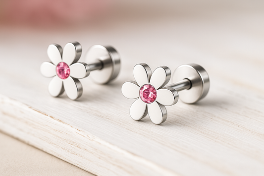 A pair of stainless steel children's flower stud earrings featuring pink cubic zirconia centres, displayed on a light woodgrain surface.