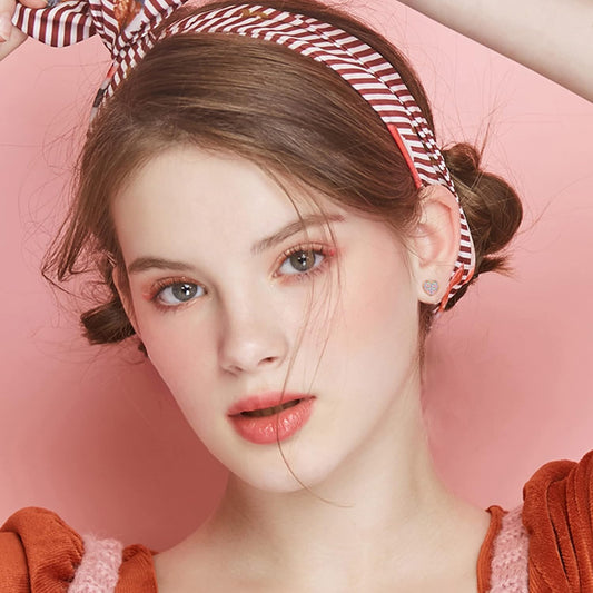 Girl wearing children's earrings, hypoallergenic steel heart studs with pink and blue CZ, showcasing a stylish look.