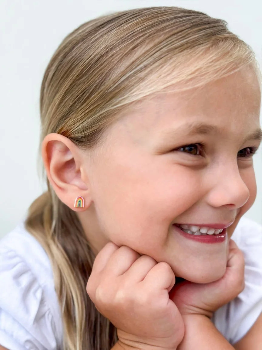 Smiling girl wearing colorful children's earrings with rainbow design, showcasing 18k gold plated surgical steel.