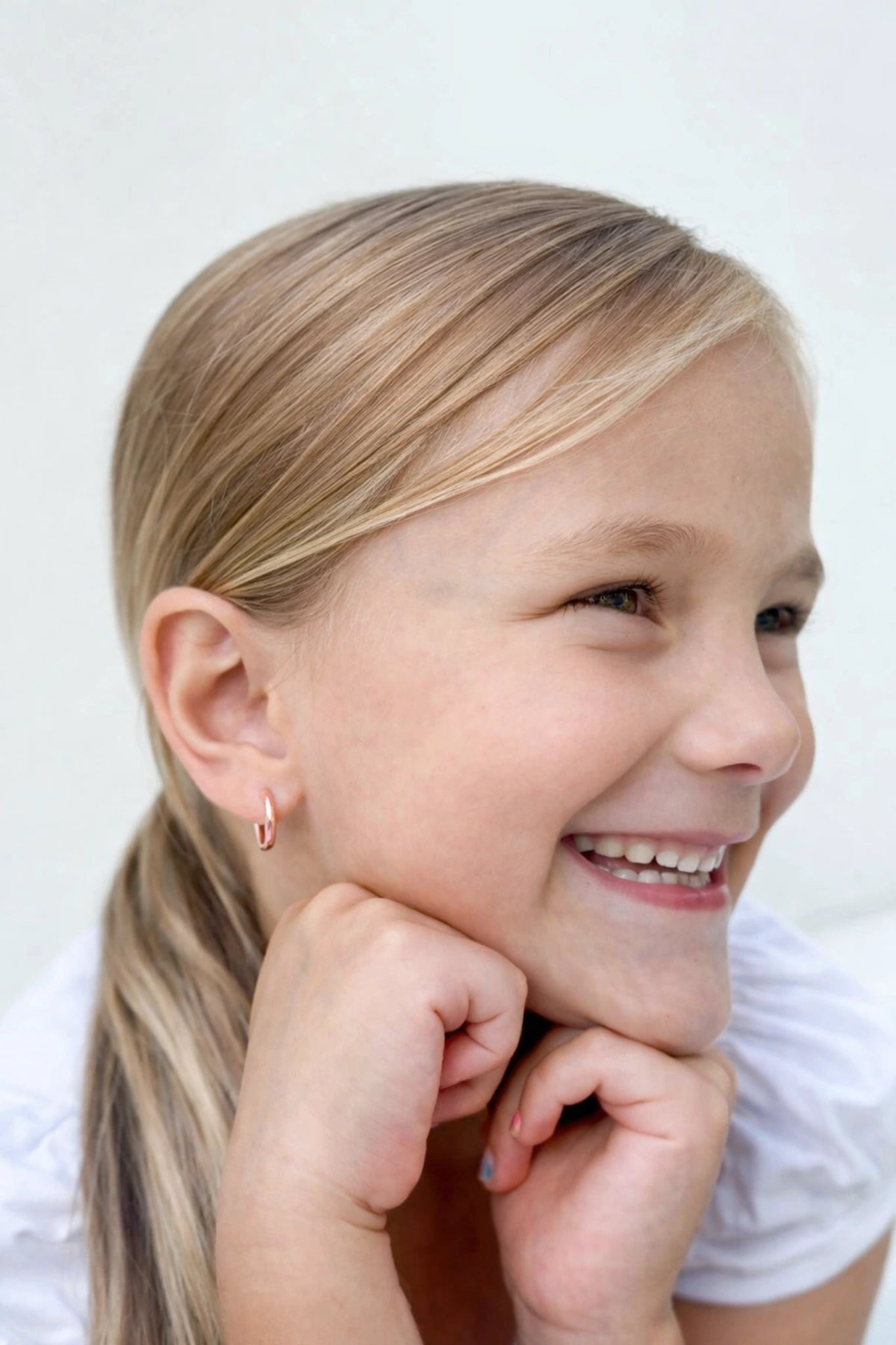Children's earrings displayed on a smiling girl, showcasing 18k rose gold plated hoop design.