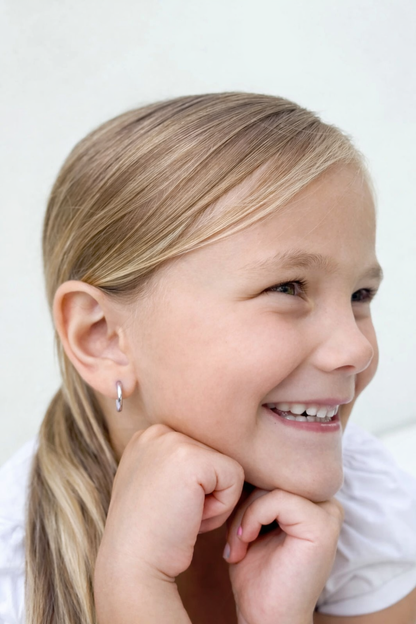 A smiling girl with long hair wearing children's earrings, showcasing 316L surgical steel hoop earrings.