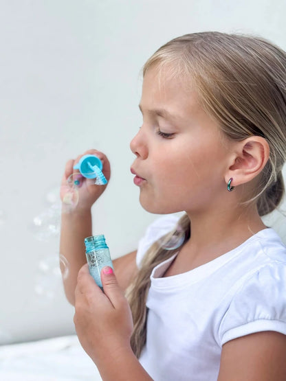 Girl blowing bubbles while wearing children's earrings made of anodised surgical steel.