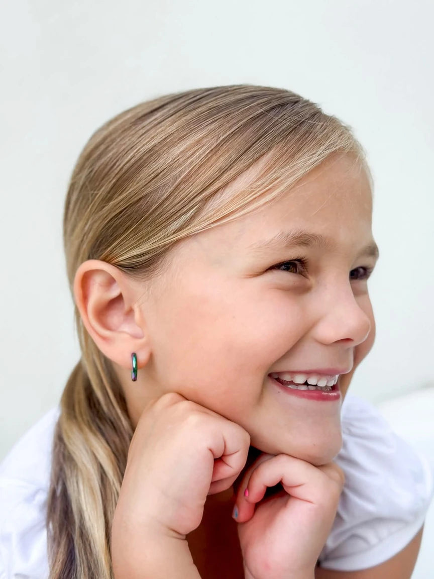 Smiling girl wearing children's earrings, showcasing anodised 316L surgical steel rainbow hoop earrings.