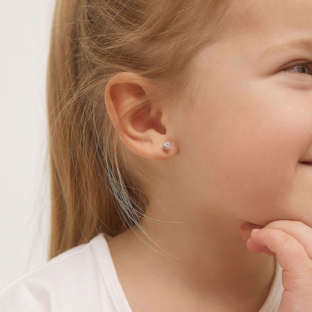 Heart earrings worn by a little girl showcasing pink cubic zirconia in solid 14k yellow gold.