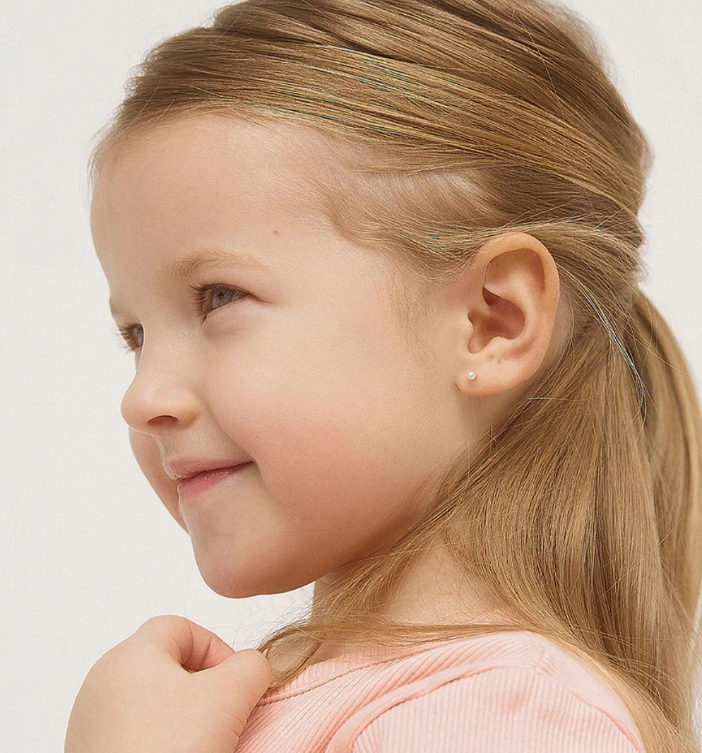 A young girl with blonde hair tied back to reveal the small white pearl earrings in her ears