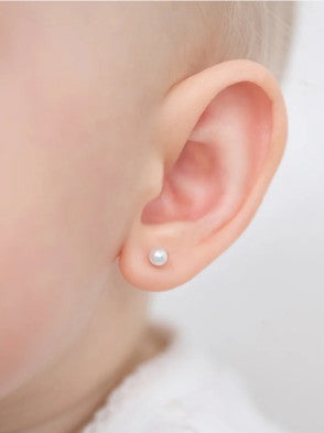 Close-up of a baby's ear with a pearl earring on a neutral background