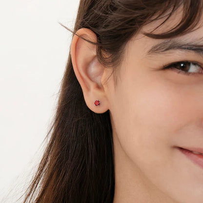 Girl wearing sterling silver birthstone stud earrings with screw backs, showcasing a charming red cubic zirconia for January.