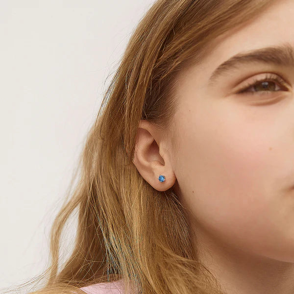 Girl wearing sterling silver birthstone stud earrings with screw backs, showcasing  sparkling blue CZ