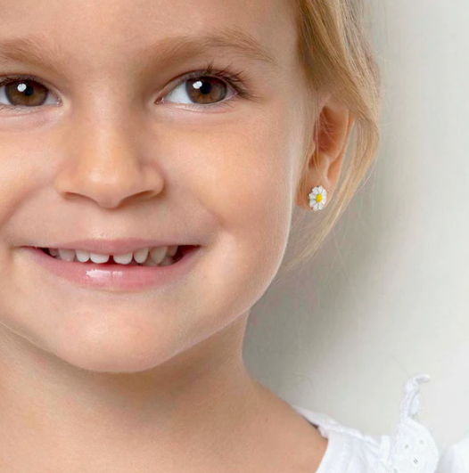 Close-up of a young girl wearing a daisy flower earring on a plain background
