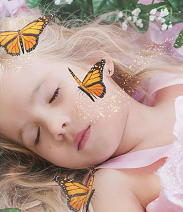 a young girl in a fairy costume laying down in a garden with star studs in her ears and butterflies in the air