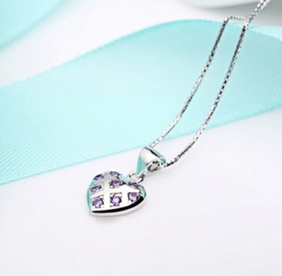 A Sterling Silver heart shaped pendant with purple cubic zirconia laid out on a soft blue and white surface