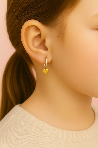 Close-up of an ear wearing a gold heart-shaped earring against a pink background