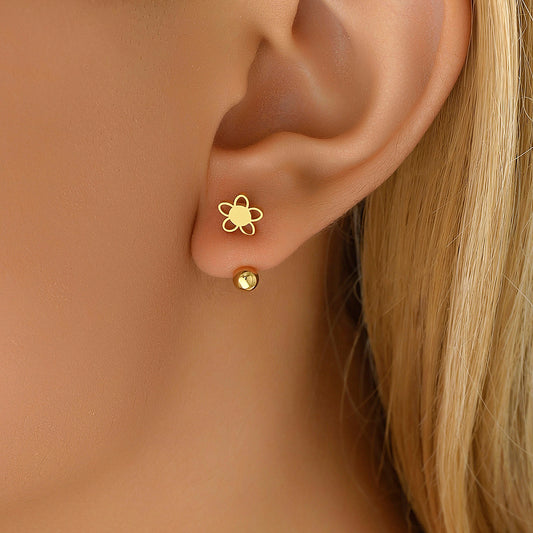A close-up image of a person's ear wearing a small 18k gold over surgical steel flower earring with a screw back.