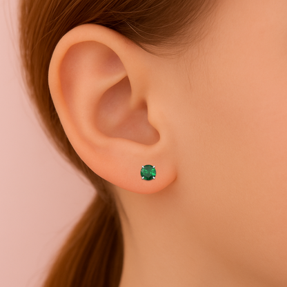 Close-up of an ear wearing a green cubic zirconia earring on a pink background
