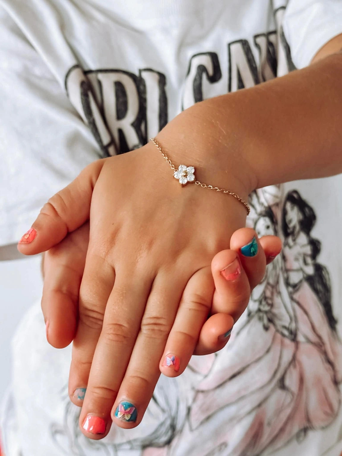 Children's bracelets featuring a child's hand wearing a 18k gold plated floral charm bracelet.