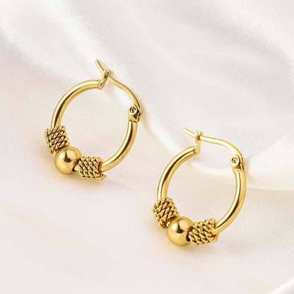 A pair of gold-colored hoop earrings with intricate designs and textures on the hoops, displayed against a white silky background.
