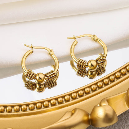 A pair of gold-coloured hoop earrings with intricate designs and textures on the hoops, displayed against a white silky background and gold framed mirror
