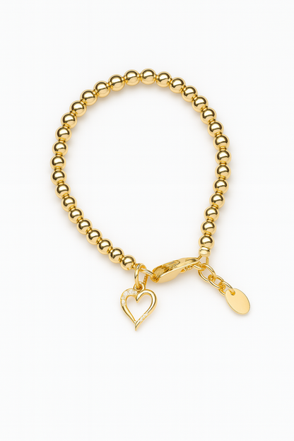 High-resolution product image of a gold beaded bracelet on a white background, featuring polished round gold beads strung into a loop with a lobster clasp, a dangling open‑heart charm accented with small crystals, and an extension chain ending in a smooth oval tag