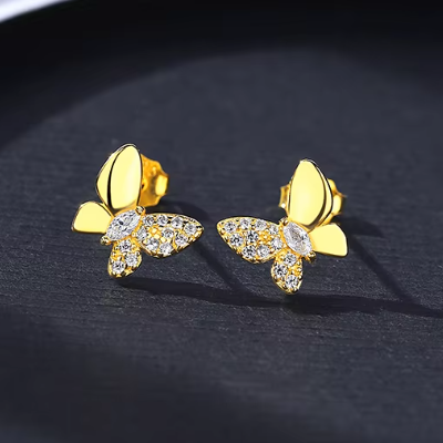 Gold butterfly earrings with clear stones on a dark background