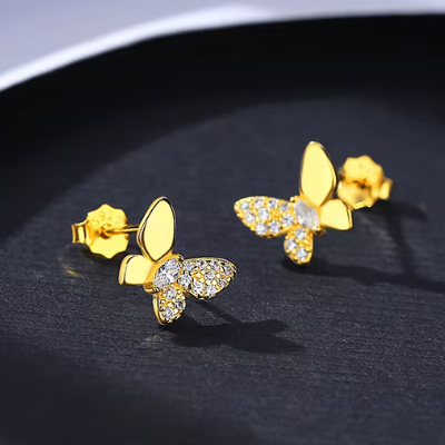 Gold butterfly earrings with clear stones on a dark surface