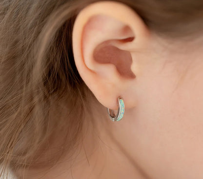 Close up image of sterling silver huggie hoops with opal inlay featured in the ear of a little girl