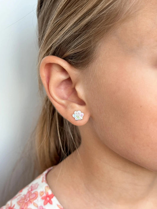 Children's earrings featuring colorful rainbow CZ paw print studs on a young girl's ear.