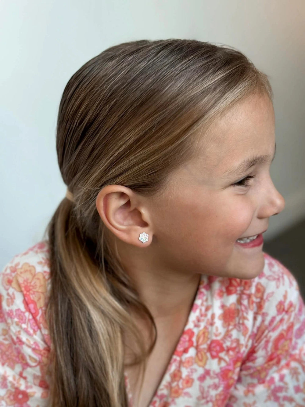 A smiling girl wearing children's earrings made of 925 sterling silver with rainbow paw print studs.