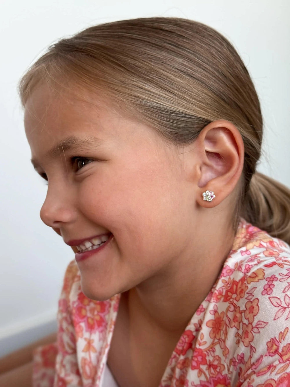 A young girl smiling while wearing children's earrings featuring a colorful paw print design.