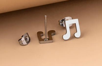 Pair of stainless steel musical note stud earrings displayed on a soft, light lifestyle background.