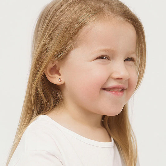Smiling young girl wearing 14k solid rose gold ball stud children's earrings with screw backs.