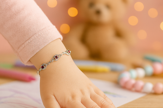 Child's hand wearing a silver bracelet with red stones, with a teddy bear and coloring books in the background.