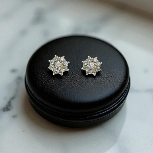 Pair of silver flower-shaped earrings on a black round container against a marble background