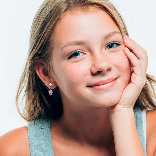 A young blonde girl with silver ball stud earrings with dangling pink cubic zirconia heart charms in her ears