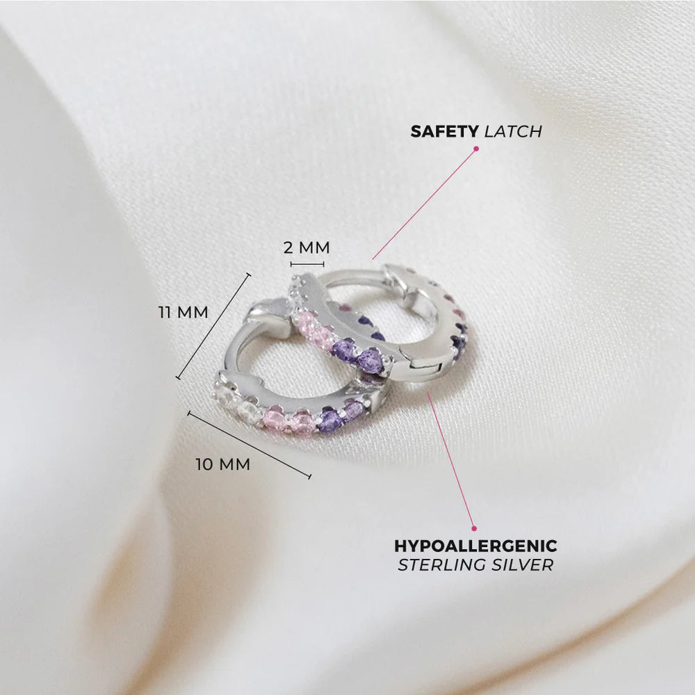 Children's earrings featuring sterling silver huggie hoops with pink and purple cubic zirconia, showcasing safety latch and hypoallergenic design.
