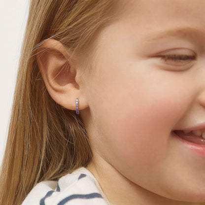 Child's smile showcasing sterling silver paved CZ huggie hoop earrings in pink and purple, perfect children's earrings.